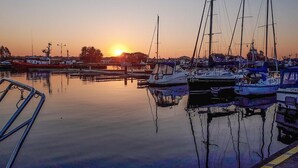 Un port de plaisance où des bateaux sont amarrés sur une étendue d'eau calme, au coucher du soleil.