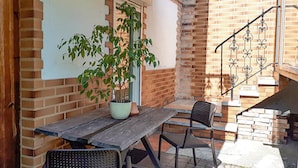 Une terrasse avec une table en bois et deux chaises, un pot de fleurs et un mur en briques.