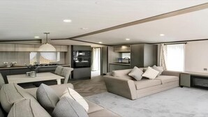 Ein modernes Wohnzimmer mit einer Couch, einem Esstisch und einer Küchenzeile mit Kühlschrank und Backofen.