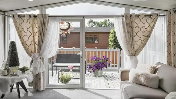 Ein Wintergarten mit einer Schiebetür, die auf eine Terrasse führt. Darin befinden sich ein weißes Sofa und ein kleiner Tisch mit Dekorationen.