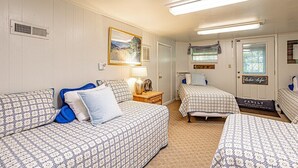 A bedroom with two beds, a nightstand, a lamp, a painting, and a door with a sign. - Grandville at Rumbling Bald (Lake Lure)