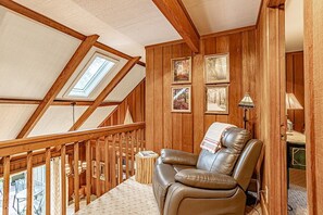Ein gemütliches Zimmer mit schrägen Wänden, Holzwänden, einem Ledersessel und gerahmten Bildern.