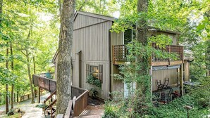 A treehouse with a wooden exterior, a wooden deck, and a small balcony. - Grandville at Rumbling Bald (Lake Lure)