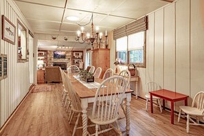 Ein Essbereich mit Holztisch und Stühlen, einer Chandelüster und Blick auf die Küche im Hintergrund.