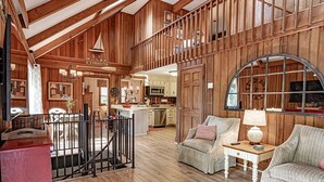 A spacious living area with a high ceiling, wooden walls, a staircase, and a kitchen in the background. - Grandville at Rumbling Bald (Lake Lure)