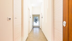 A hotel hallway with a wooden floor, white walls, and a glass door at the end. - Solaris Suites  (Naples)