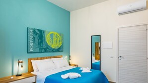 A modern bedroom with a bed, a nightstand, a mirror, and a door. - Solaris Suites  (Naples)