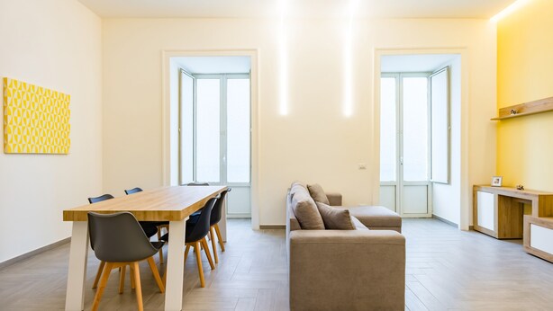 A modern living room with a wooden dining table, grey chairs, a beige sofa, and a wooden cabinet. - Solaris Suites  (Naples)