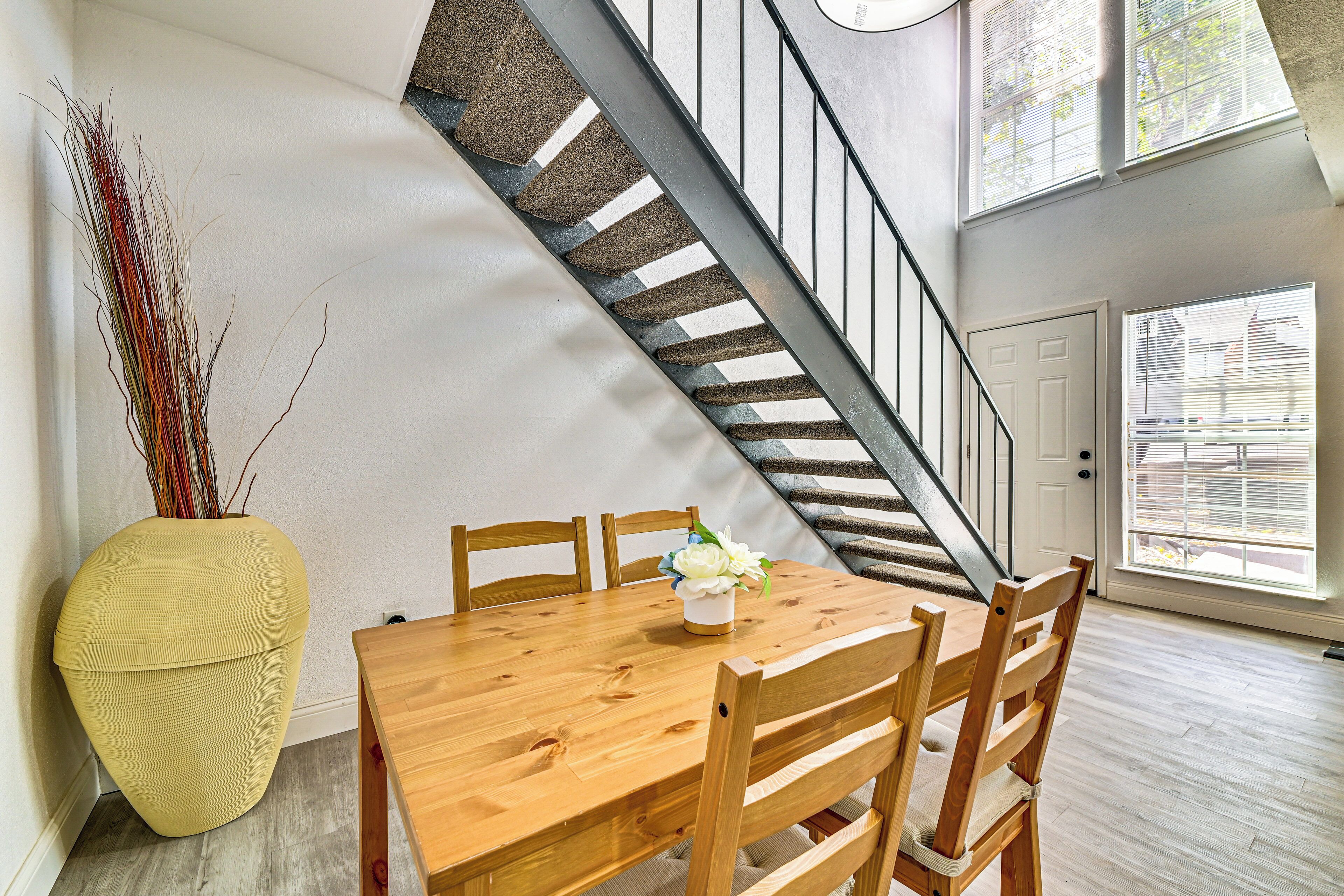 A dining area with a wooden table and chairs, a vase with flowers, and a staircase with a metal railing.