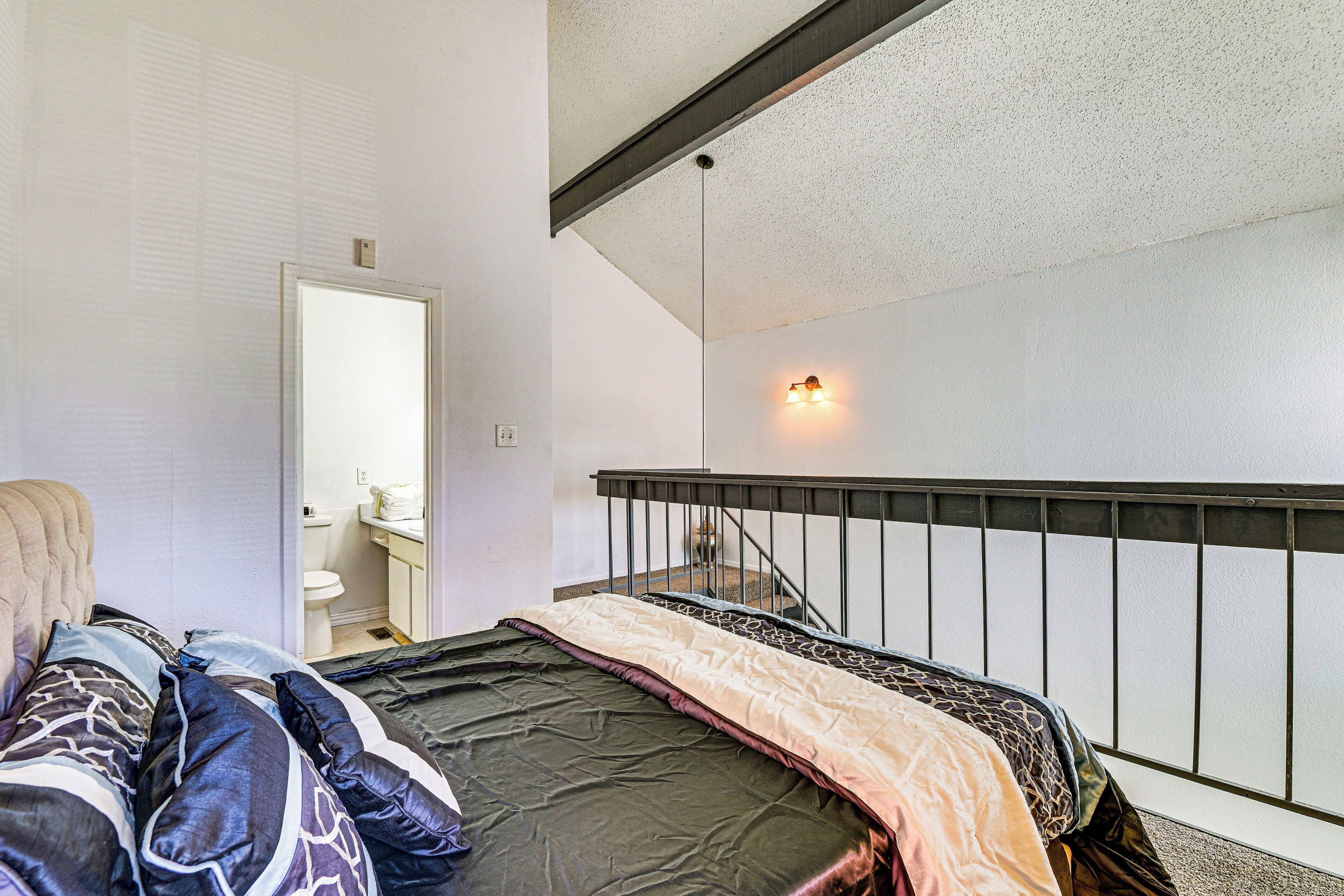 A bedroom with a bed, a chair, a bathroom, and a staircase.