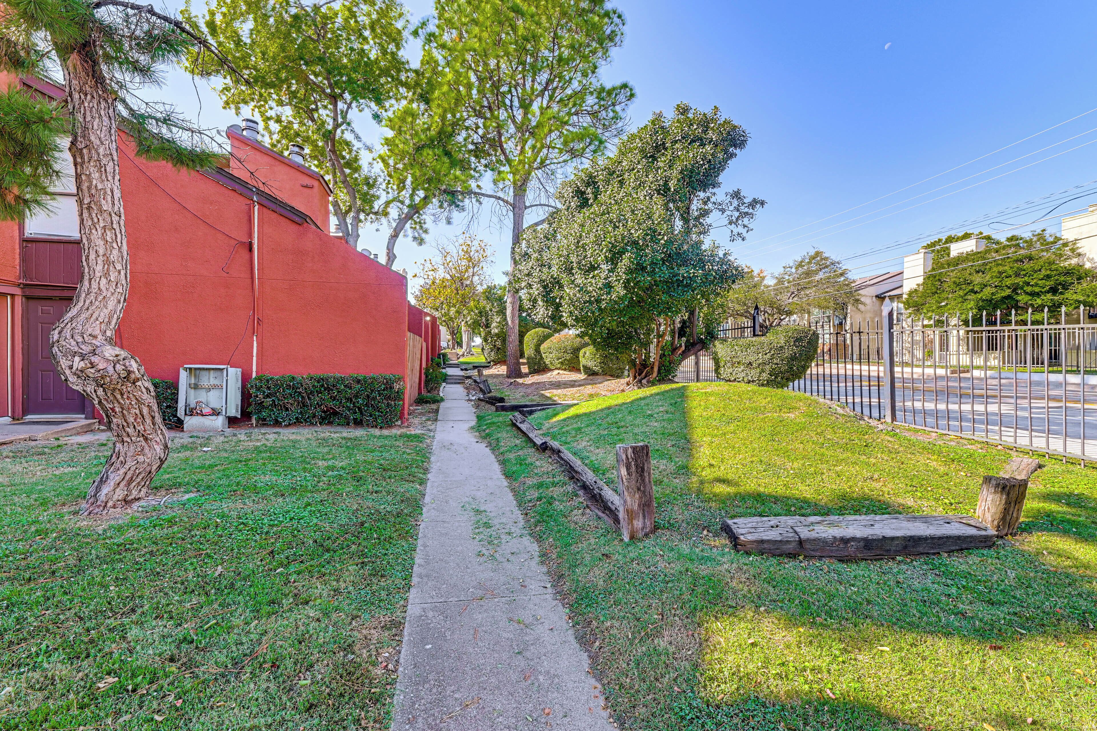 A residential street with a red building, a sidewalk, and green lawns.
