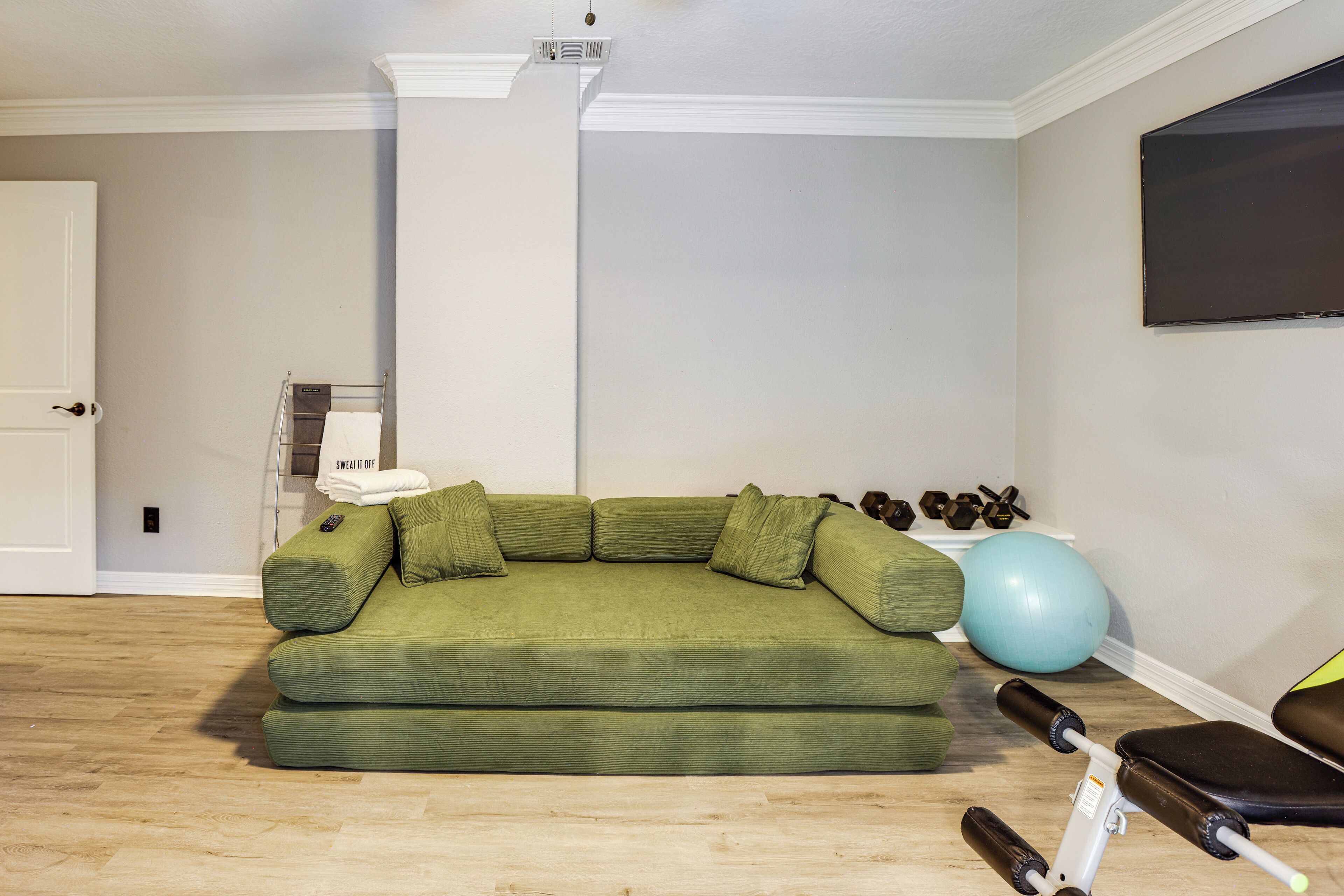 Un salón con un sofá verde, equipo de ejercicio y una pelota de ejercicio azul.