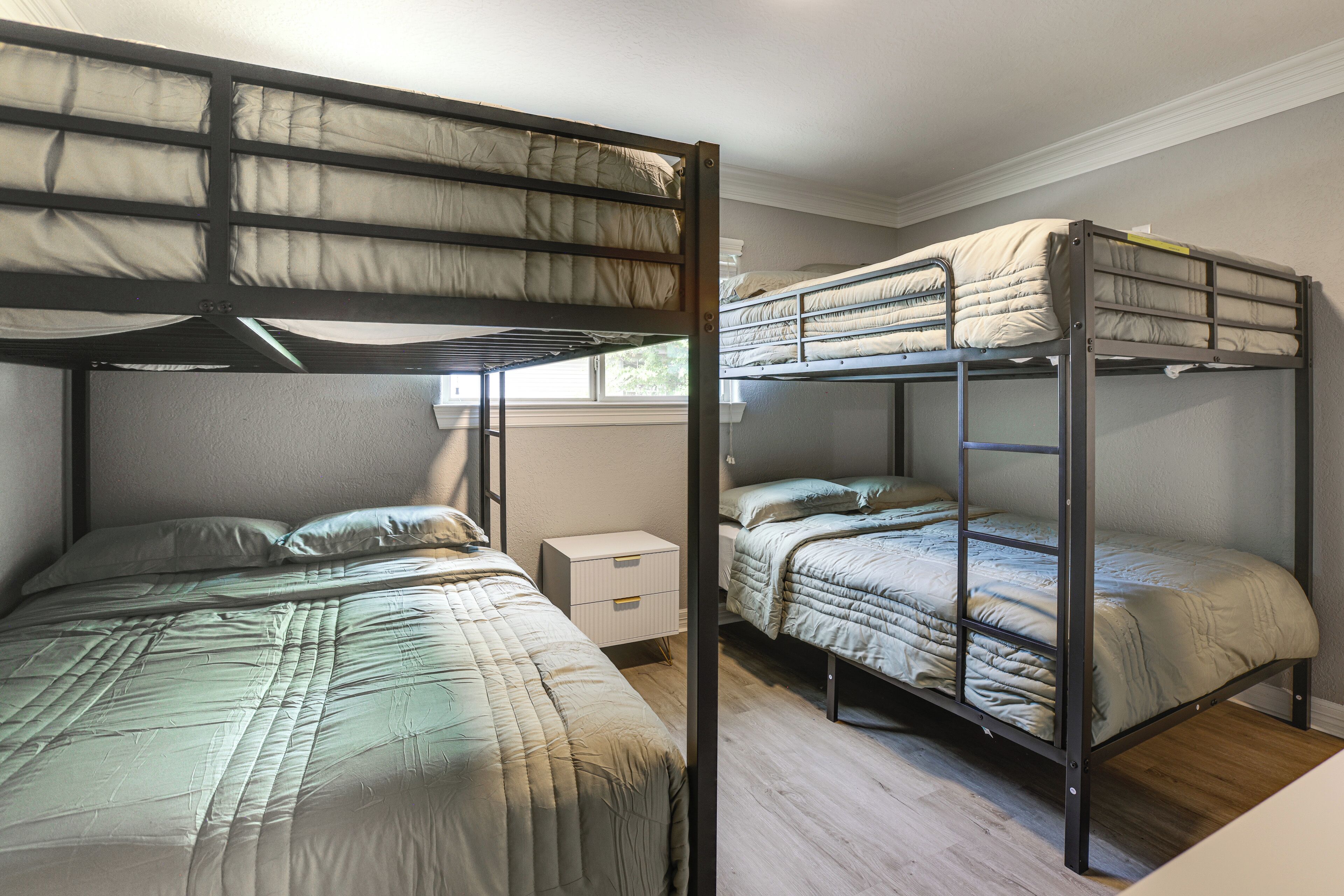 Ein Schlafzimmer mit Etagenbett, Holzboden, einem kleinen Nachttisch und einem Fenster.