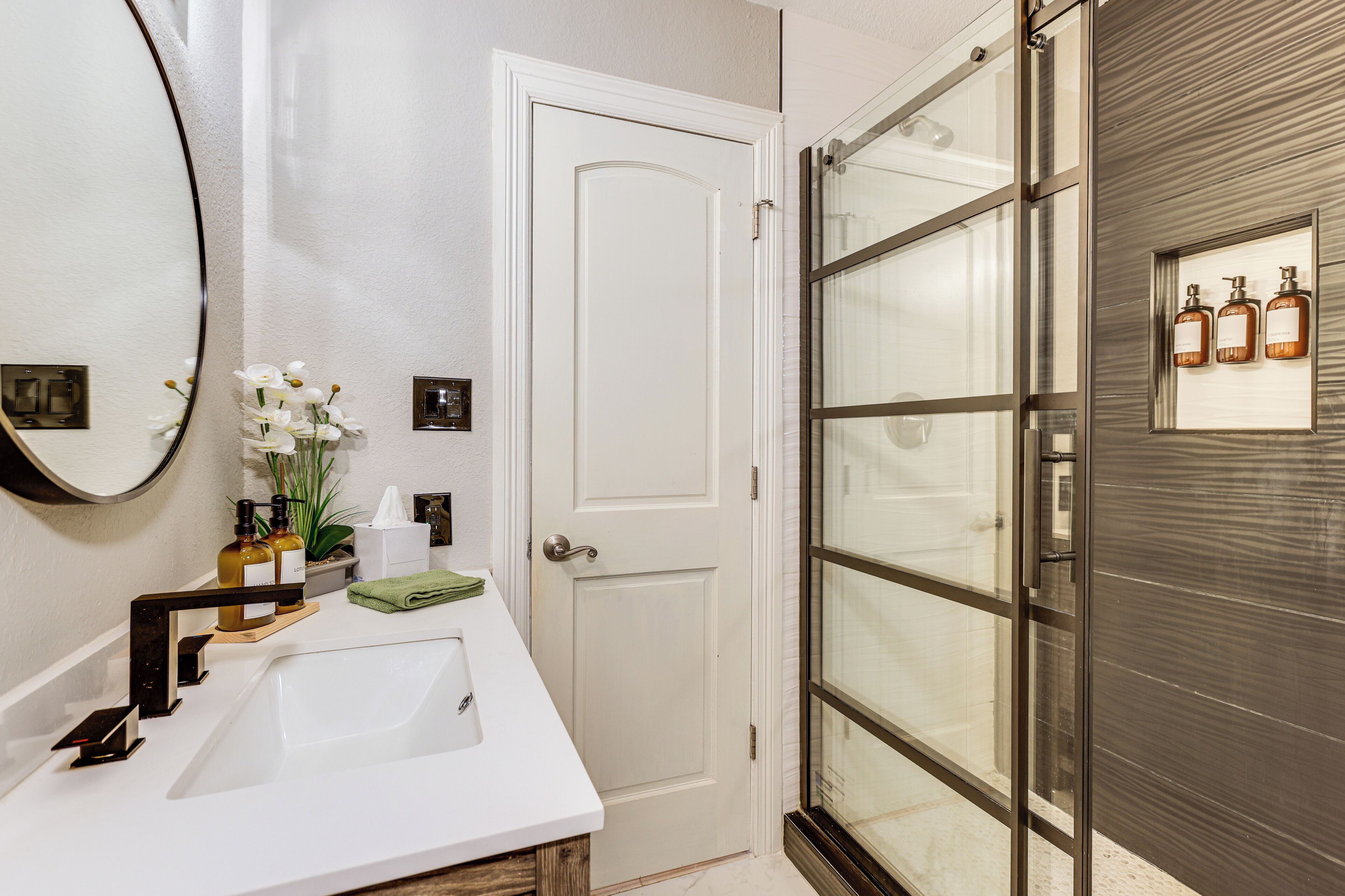 A bathroom with a white sink, a large mirror, and a door leading to a shower area.