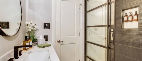 A bathroom with a white sink, a large mirror, and a door leading to a shower area.