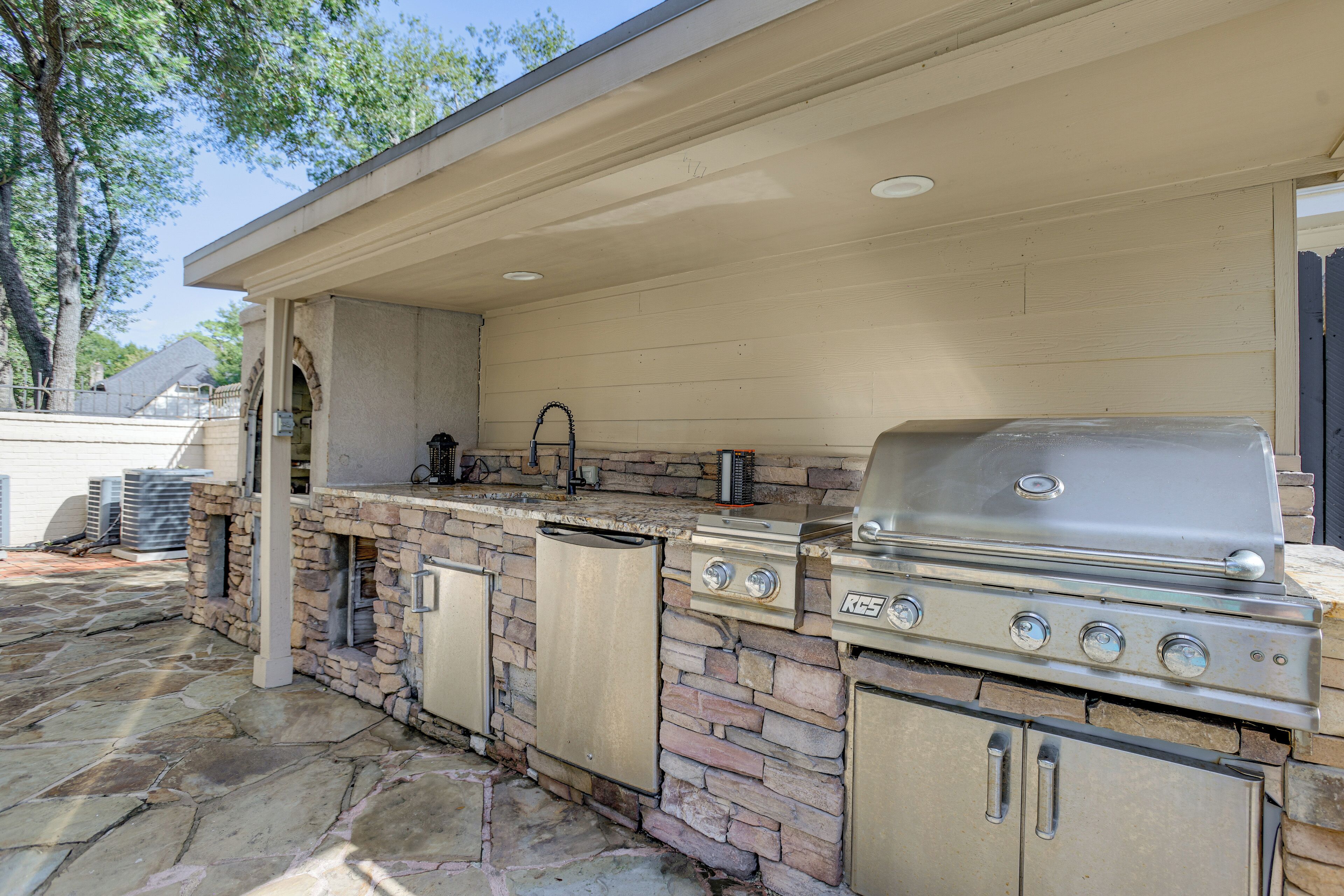 An outdoor kitchen with a stone backsplash, a built-in grill, and a sink.