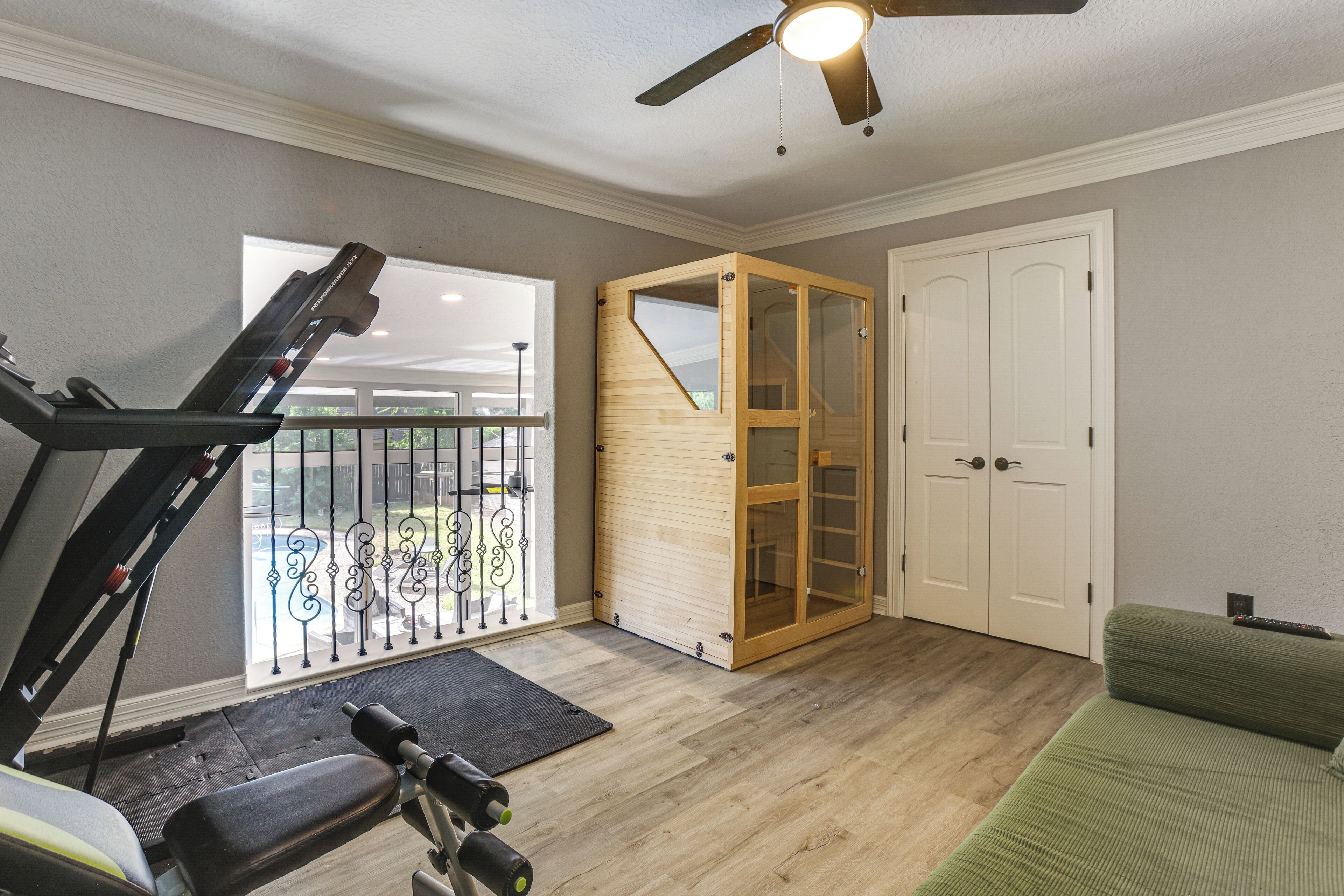 A home gym with a treadmill, exercise bike, and weights. There's a sliding glass door leading to a balcony with a railing.