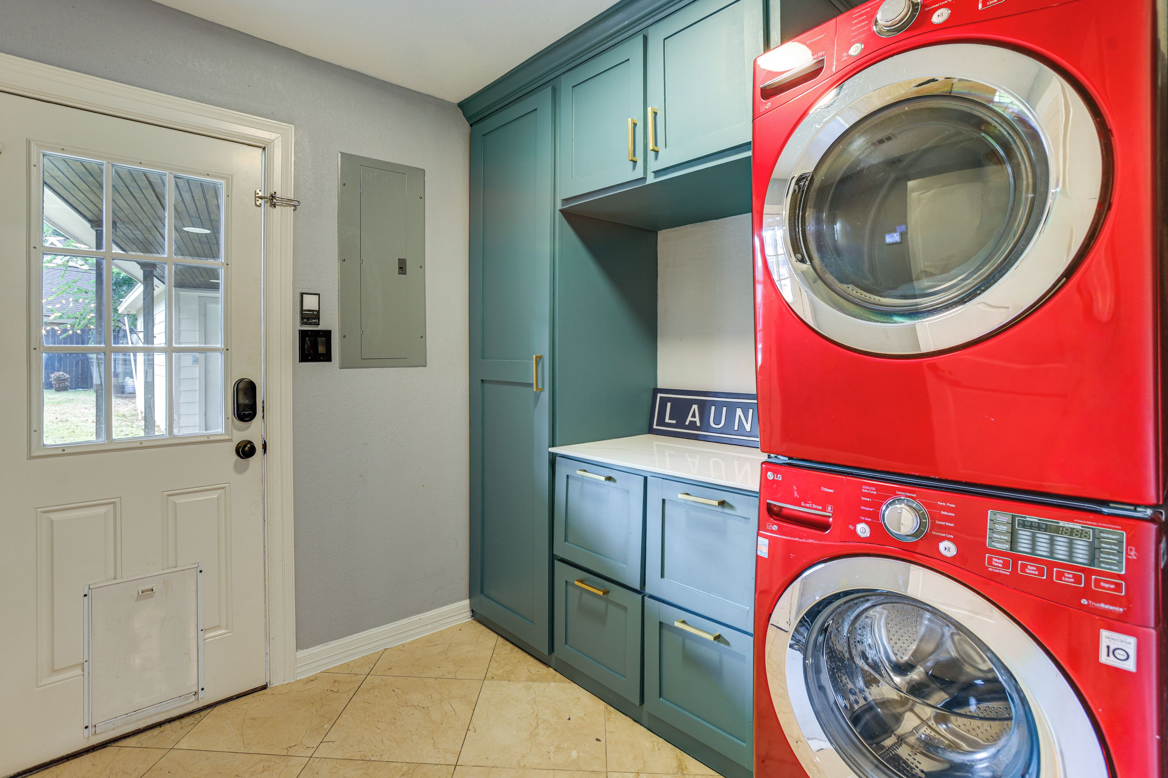 A laundry room with a red front-loading washer and dryer, teal cabinets, and a white door with a window.