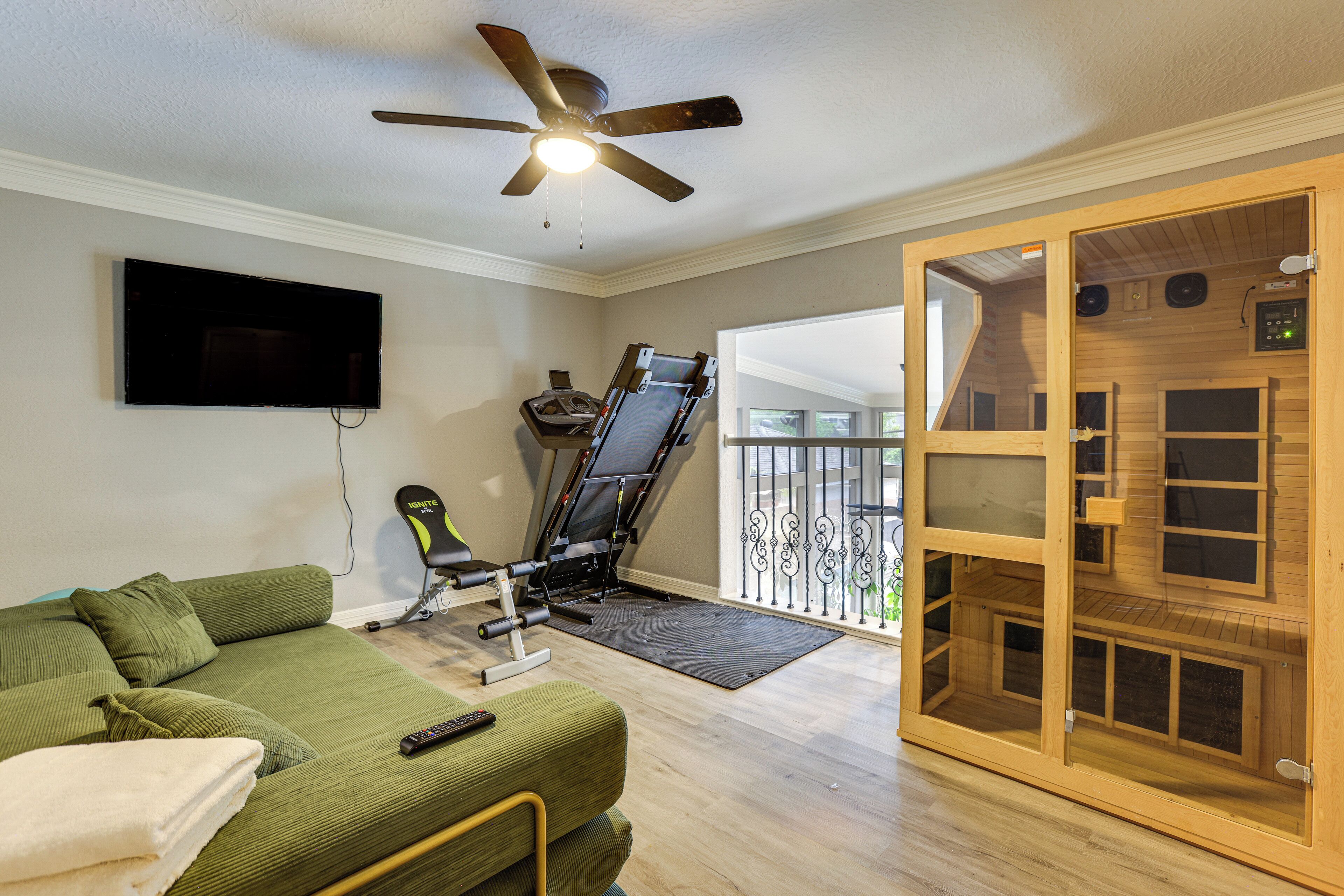 A room with a green sofa, a treadmill, a ceiling fan, and a wooden sauna.