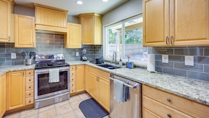 A modern kitchen with wooden cabinets, a stainless steel oven, granite countertops, and a large window providing natural light. - Work, Explore & Unwind: Convenient San Antonio Gem (San Antonio)