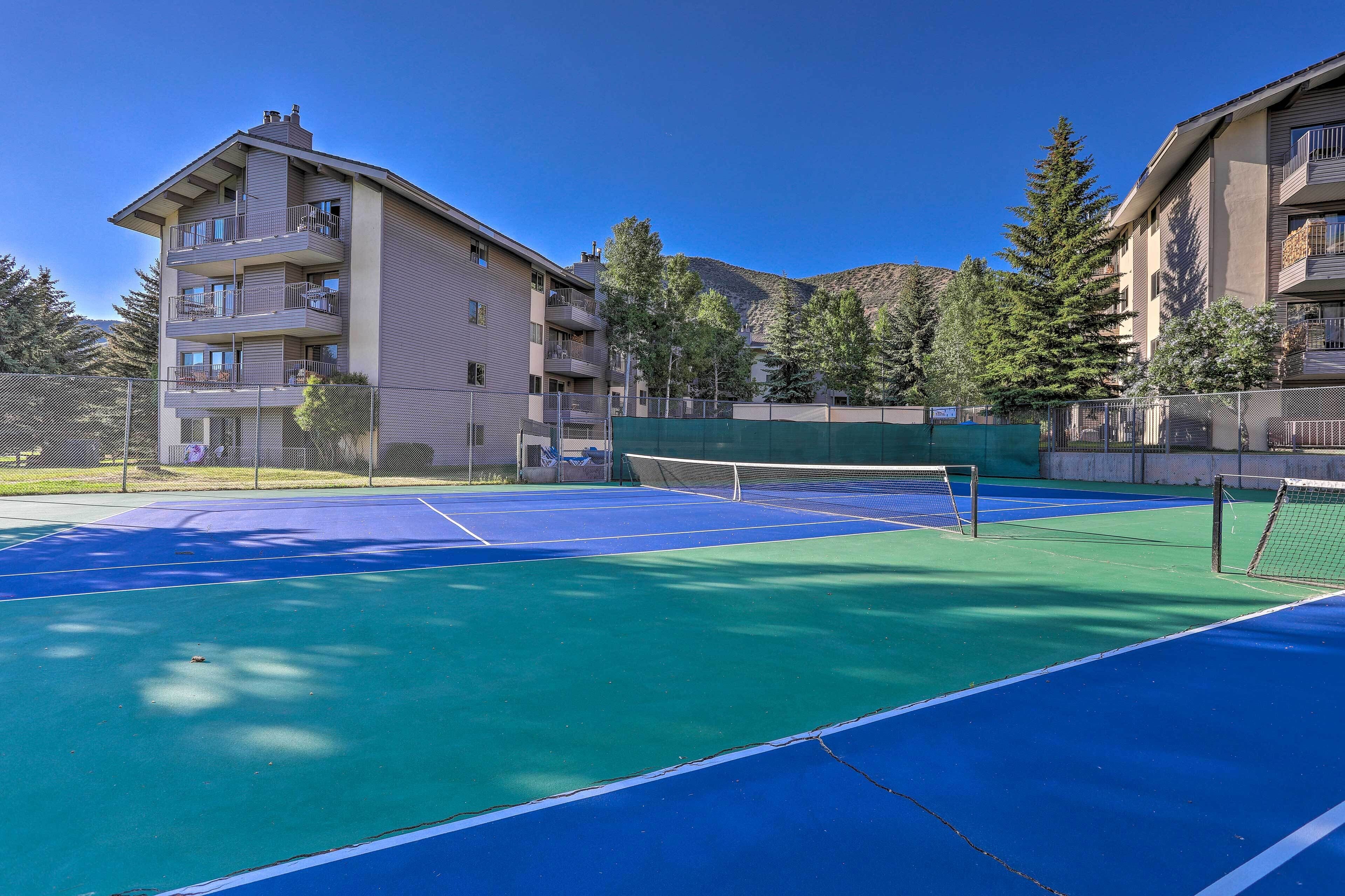 Een tennisbaan met een net, omgeven door appartementencomplexen.