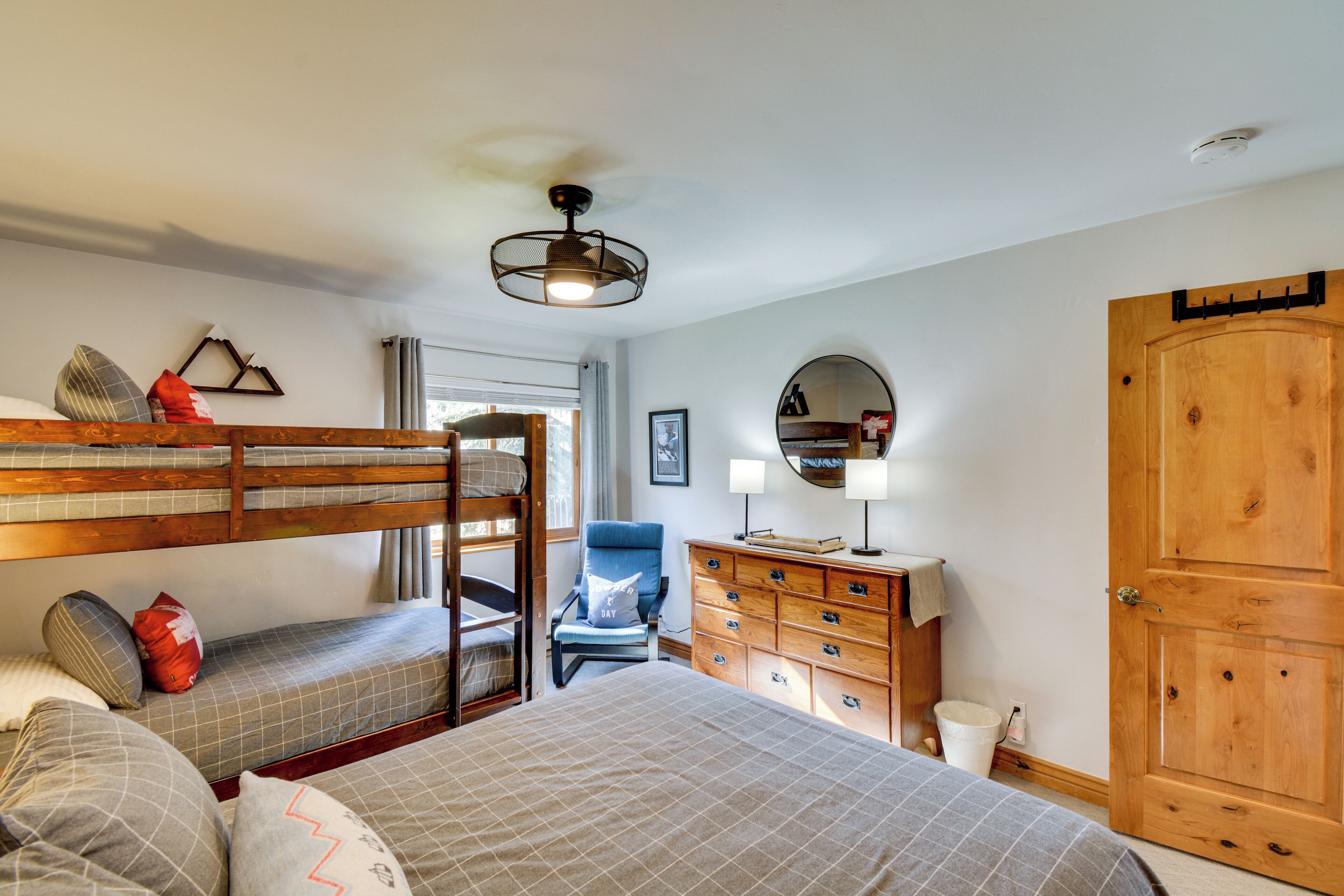 Un dormitorio con una cama litera, un escritorio, una silla, un aparador y una puerta de madera.