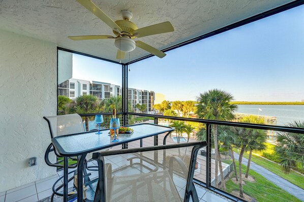 A balcony with a table and chairs, a ceiling fan, and a view of a body of water and buildings. - Riverside Marco Island Condo: Pool & Marina Access (Marco Island)