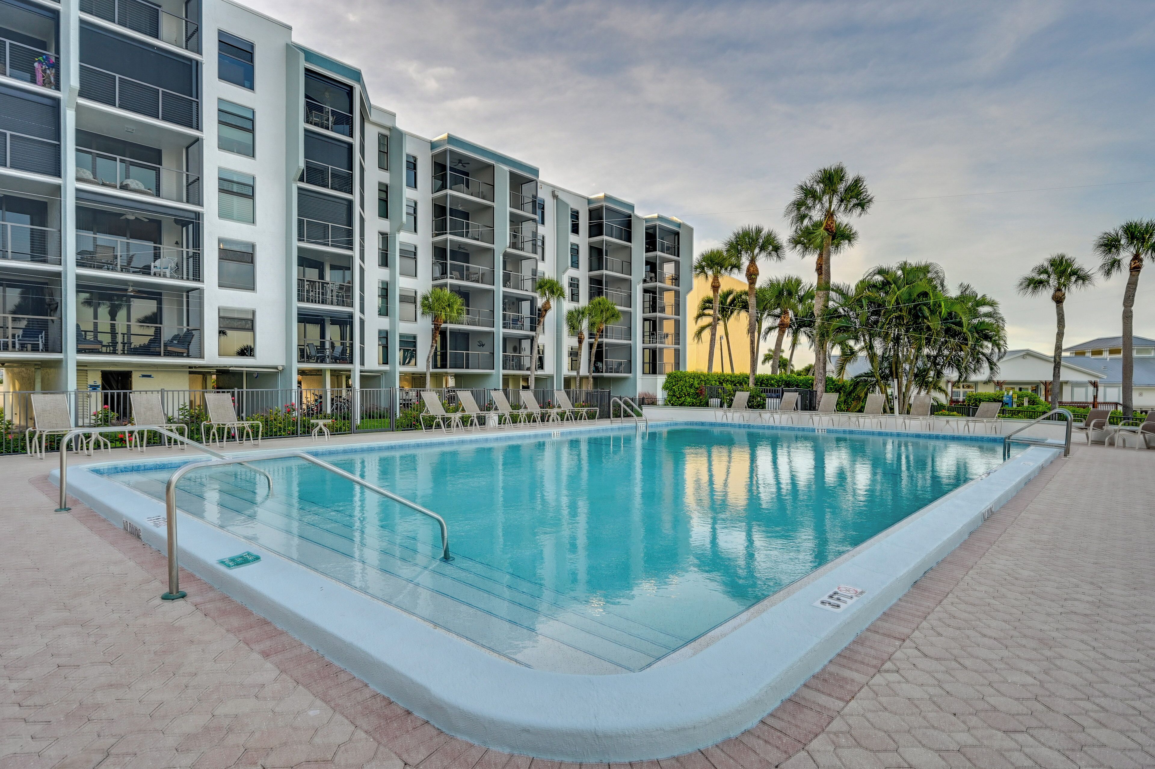 A swimming pool with lounge chairs and a modern building with balconies in the background.