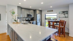 Une cuisine moderne dotée d’un grand îlot central, de meubles gris, d’appareils électroménagers en acier inoxydable et offrant une vue sur l’extérieur.