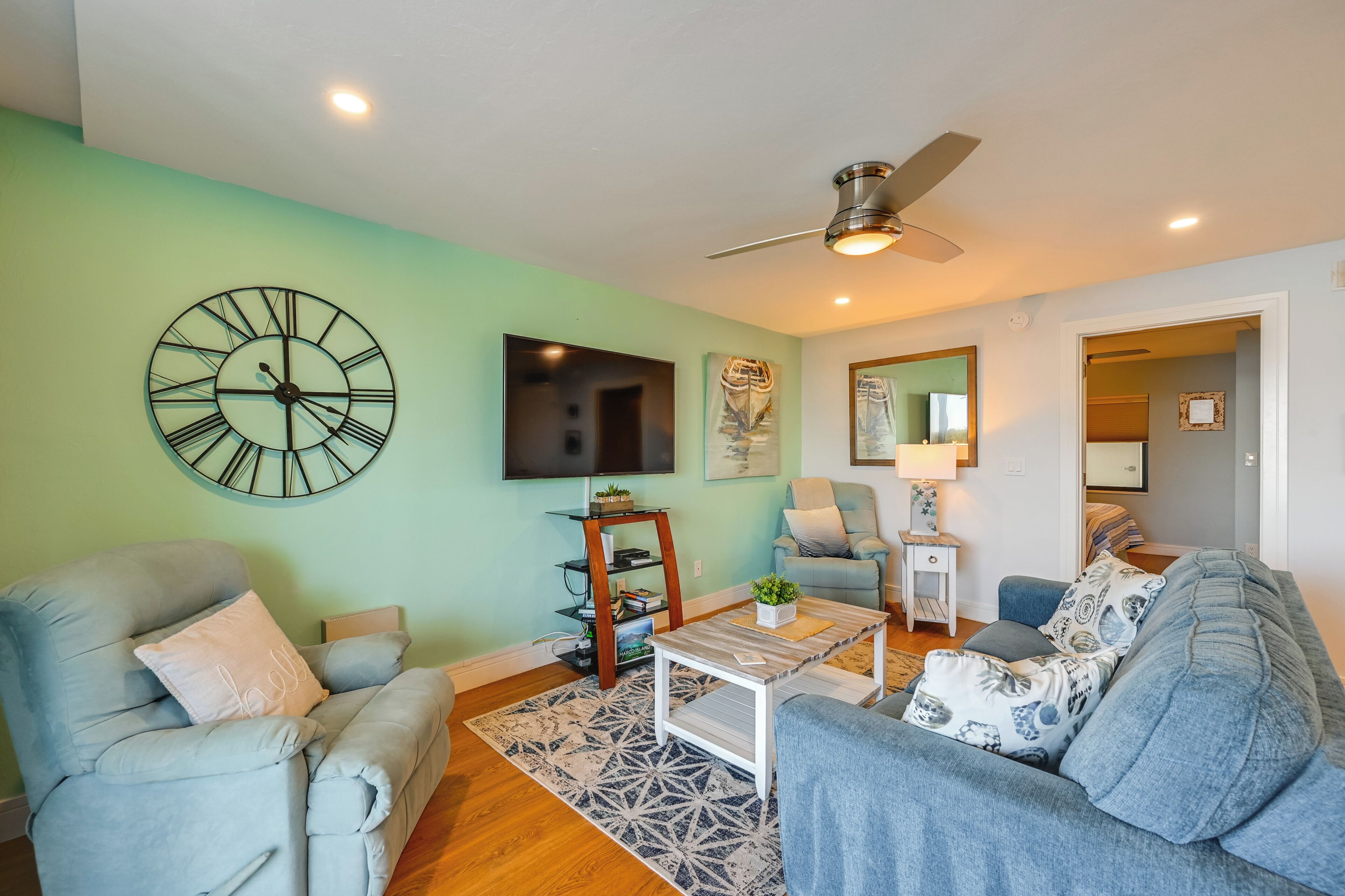 A living room with a large wall clock, a ceiling fan, and a flat-screen TV.