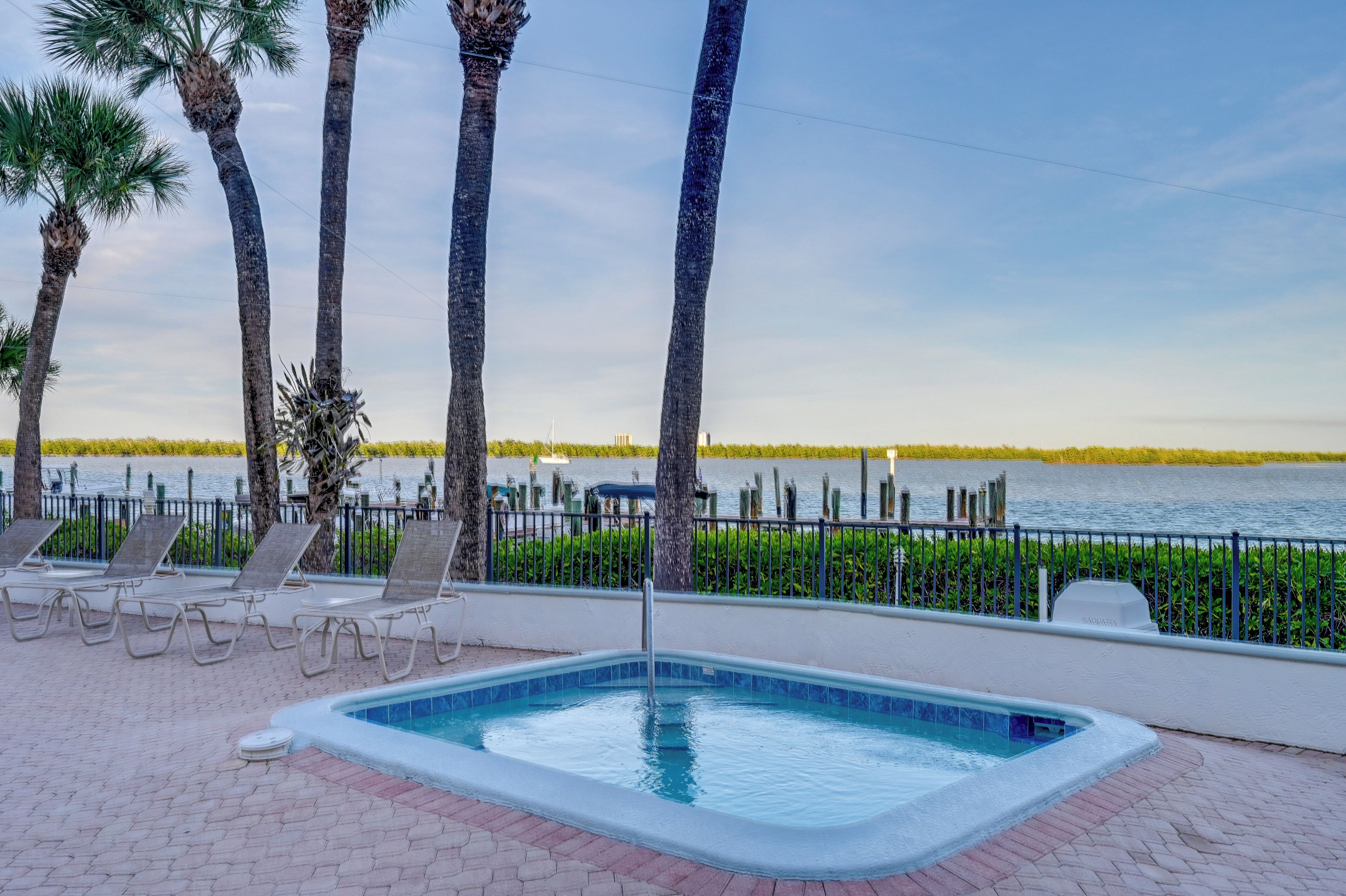 A swimming pool with lounge chairs and palm trees, overlooking a body of water.