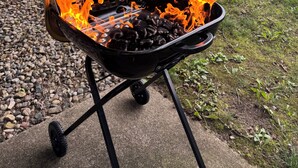 A portable grill with flames, set on a concrete surface with a grassy yard and a wooden fence in the background. - Close to Notre Dame Family And Pet Friendly  house Heat AC  

Located in Elkhart (Elkhart)