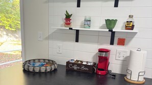 A kitchen with white tiled walls, black countertops, and stainless steel appliances. There are shelves with various items, a coffee maker, and a basket labeled "Coffee Bar". - Close to Notre Dame Family And Pet Friendly  house Heat AC  

Located in Elkhart (Elkhart)