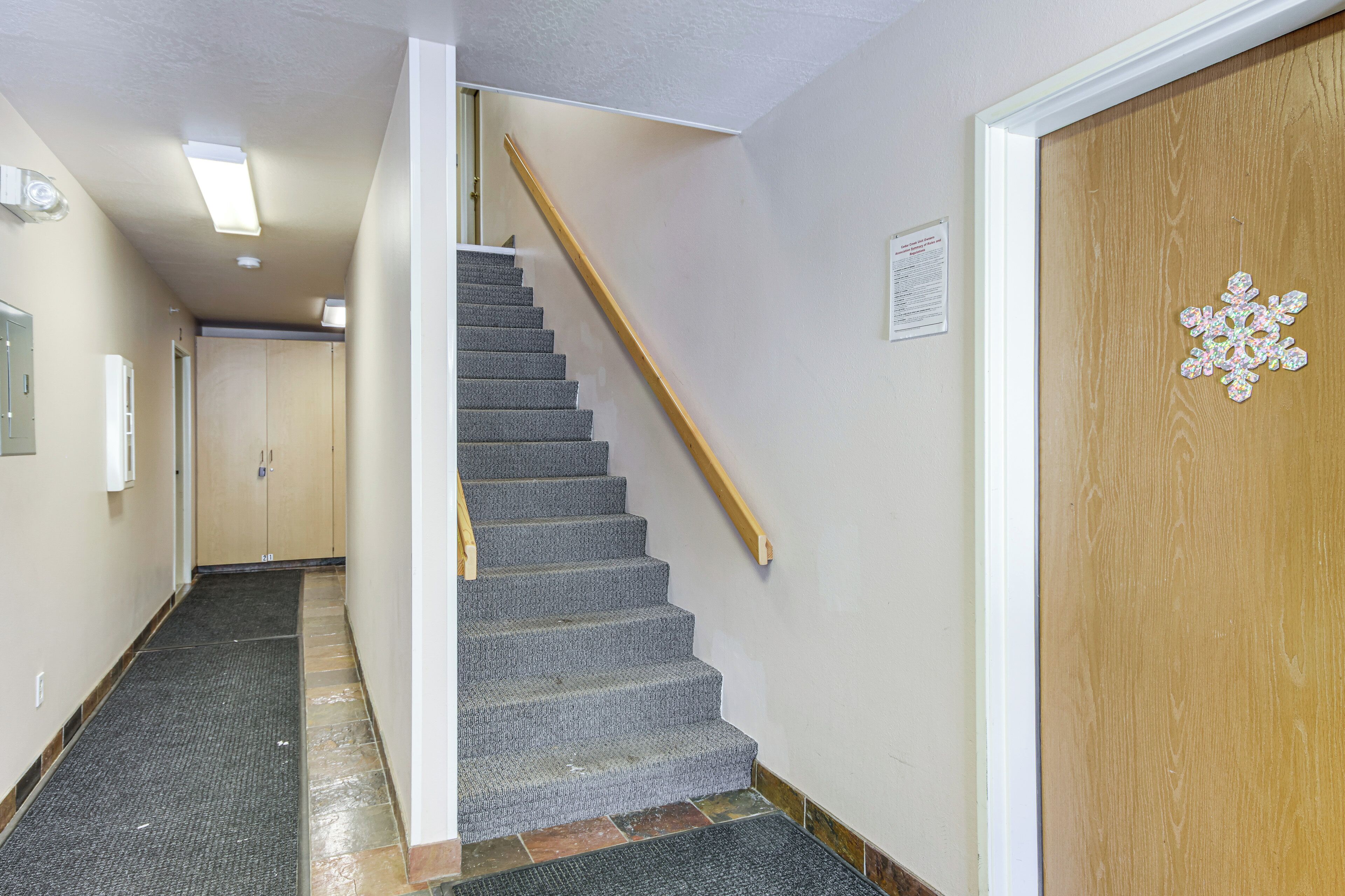 A hallway with a carpeted staircase, a wooden door with a snowflake decoration, and a wall-mounted sign.