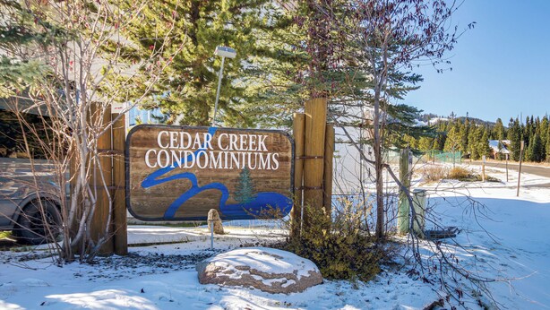 Un senyal de fusta per a Cedar Creek Condominiums amb un disseny d'ocell blau.