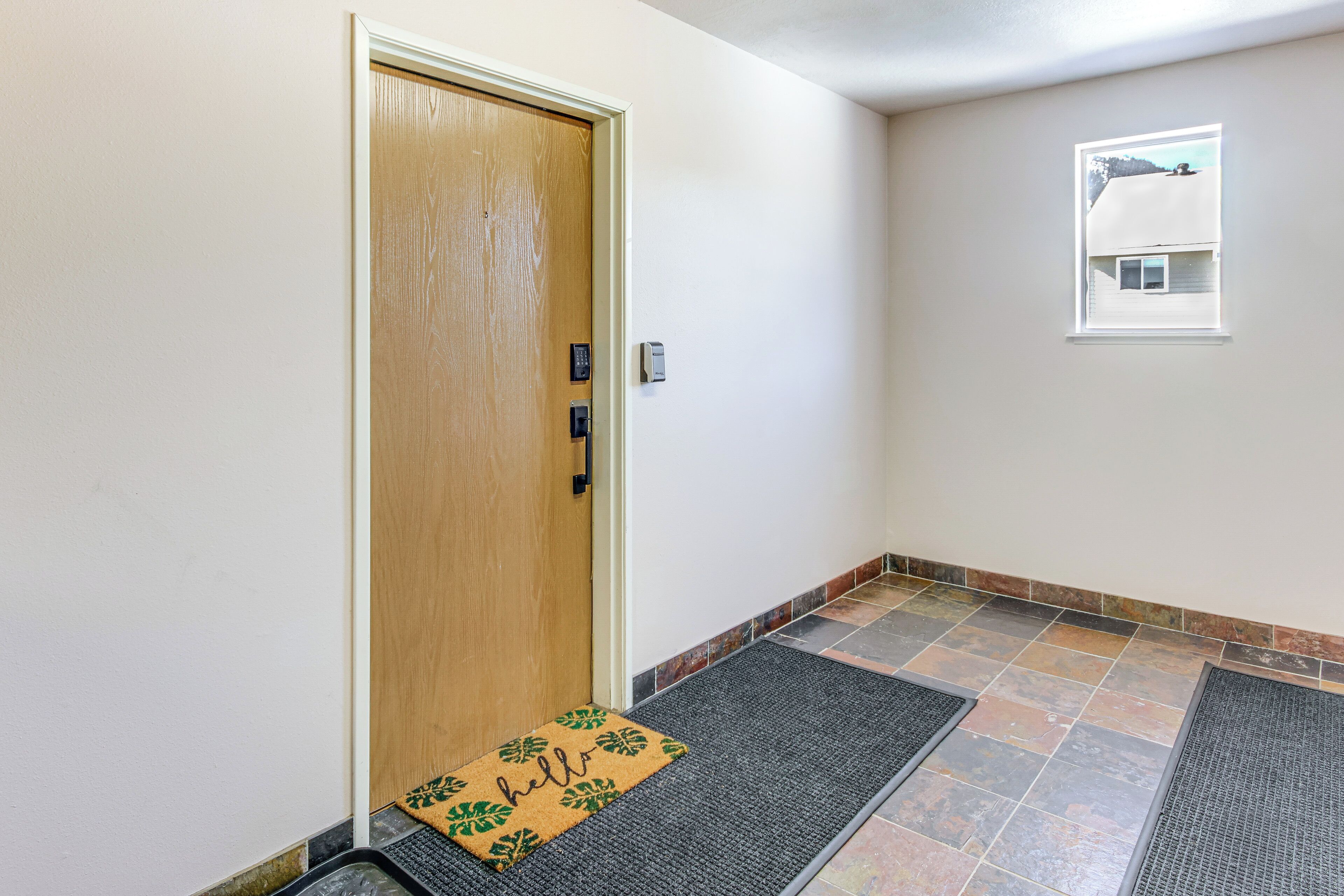 Um corredor com porta de madeira, tapete de entrada, uma pequena janela e chão de azulejos.