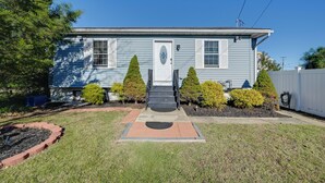 A single-story house with a front porch, a small garden area, and a clear blue sky.