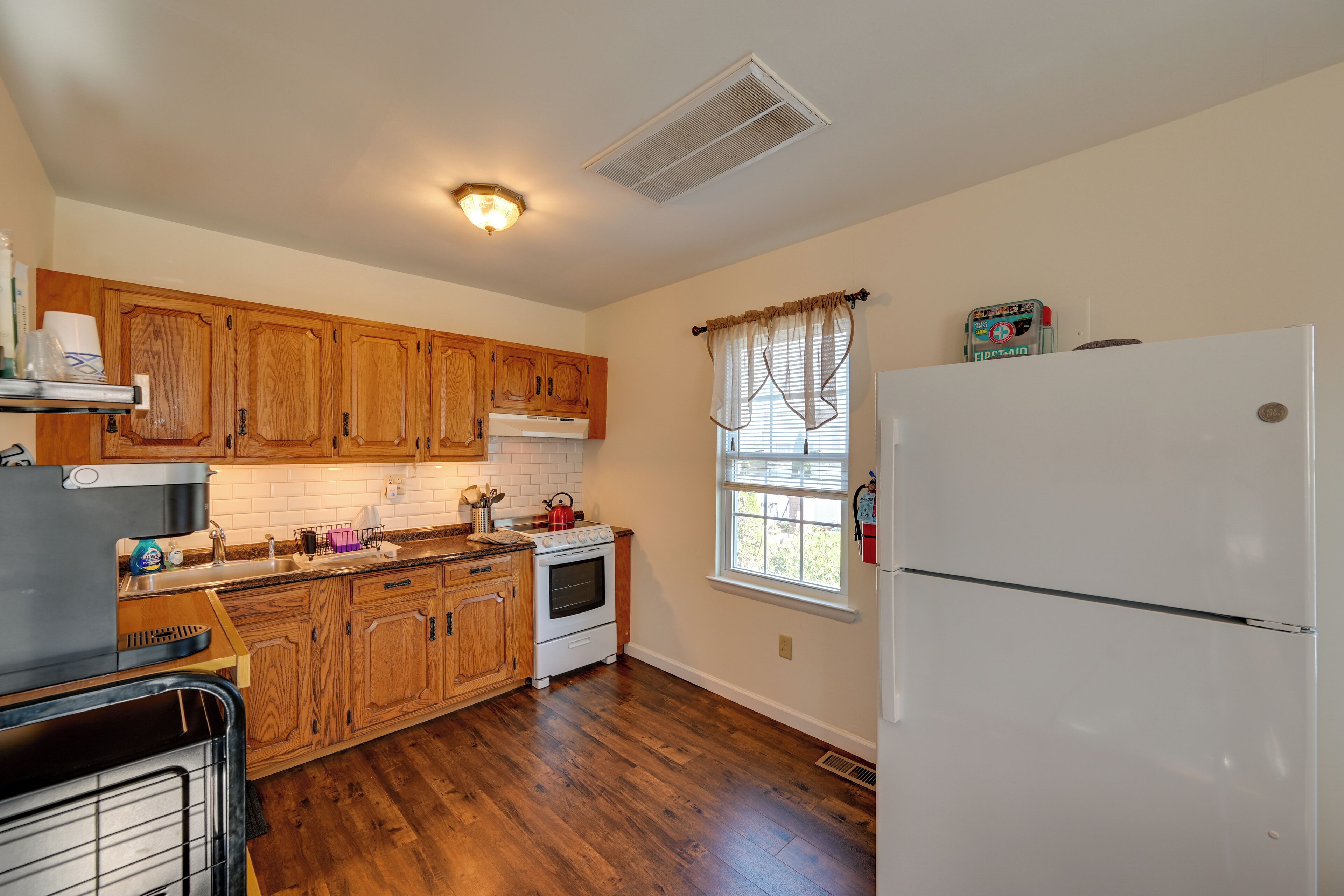 A kitchen with wooden cabinets, a white refrigerator, and a window with curtains.