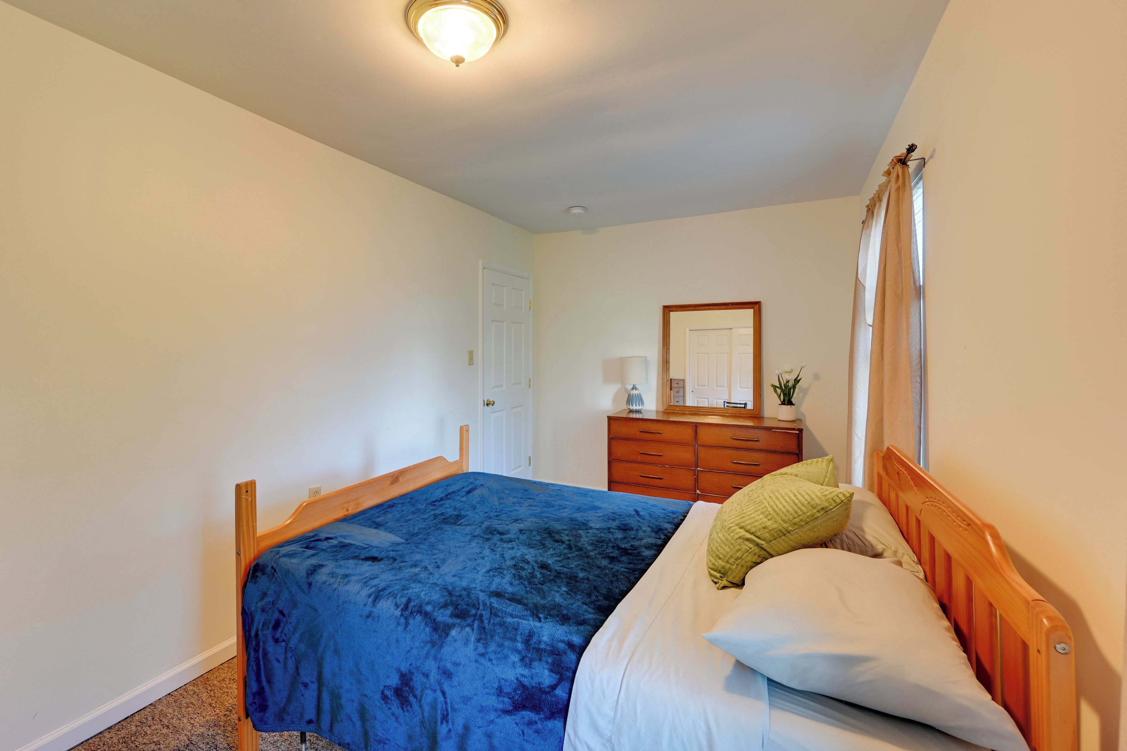 A bedroom with a wooden bed, a dresser, a mirror, and a window with curtains.