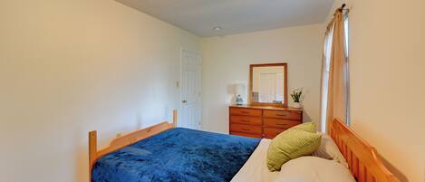 Un dormitorio con cama de madera, cómoda, espejo y ventana con cortinas.