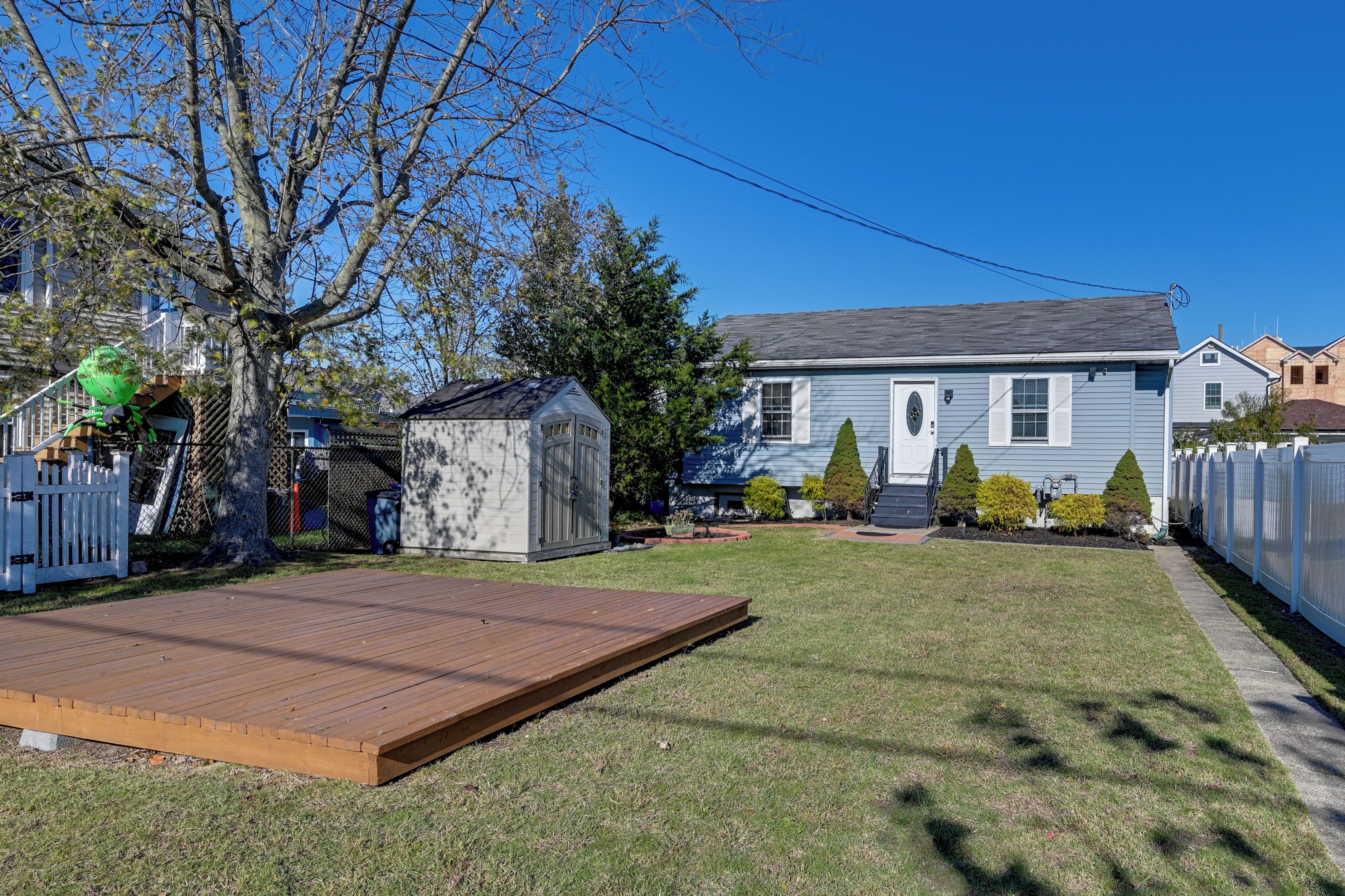 A backyard with a wooden deck, a shed, and a house with a gray roof.