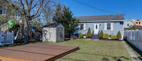 A backyard with a wooden deck, a shed, and a house with a gray roof.