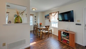 A dining area with a wooden table and chairs, a TV mounted on the wall, and a bookshelf with books and decorative items.