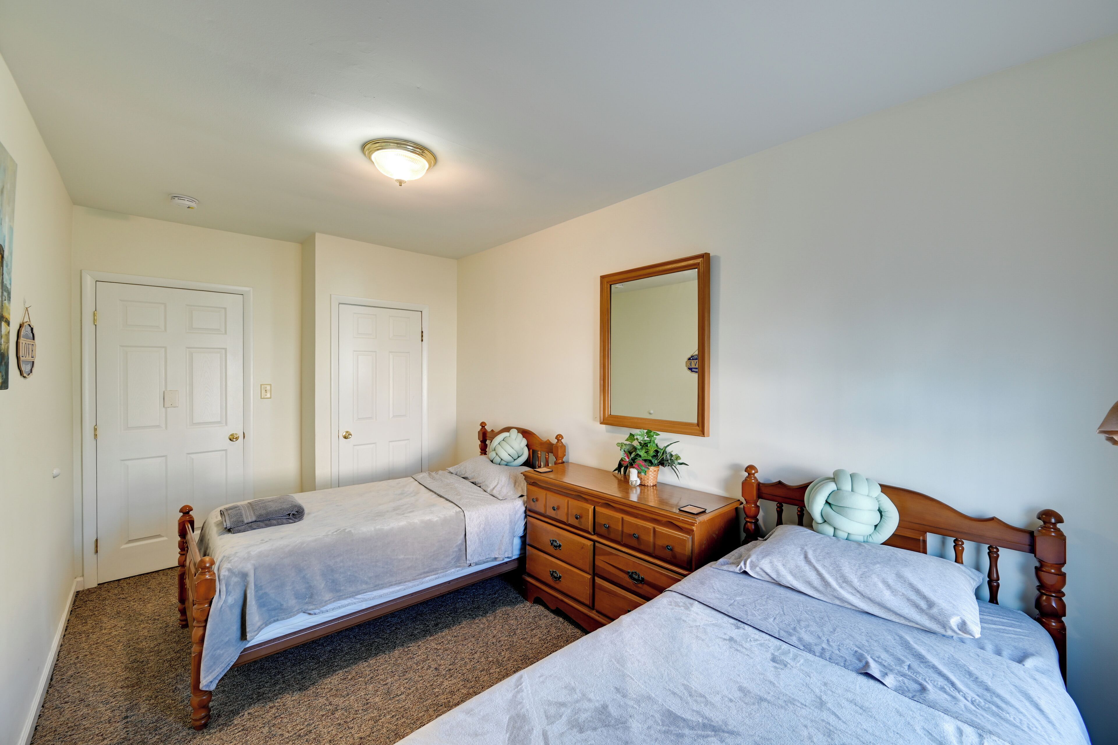 A bedroom with two single beds, a wooden dresser, a mirror, and a door.