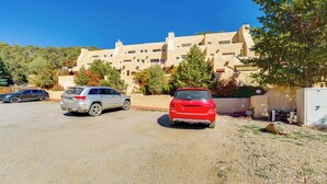 Un parcheggio con diverse auto, un edificio con molte finestre e balconi, e un cielo azzurro intenso.