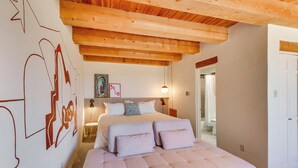 Una camera da letto con un letto grande, travi in legno a soffitto, una parete con arte astratta e una lampada da comodino.