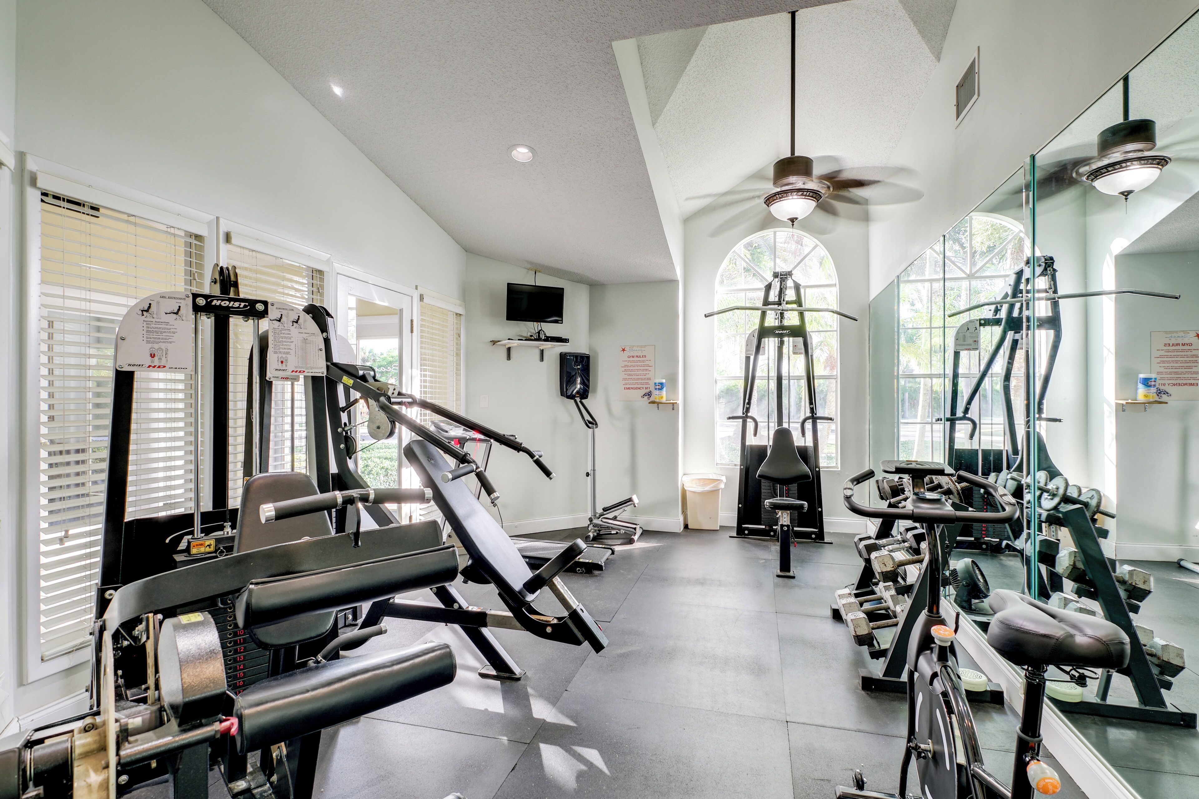 A gym with various exercise equipment, a television, and large windows allowing natural light.