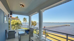 A covered balcony with wicker furniture, a view of the sea, and a palm tree. - Riverfront Fort Myers Luxury Home w/ Heated Pool! (Fort Myers)