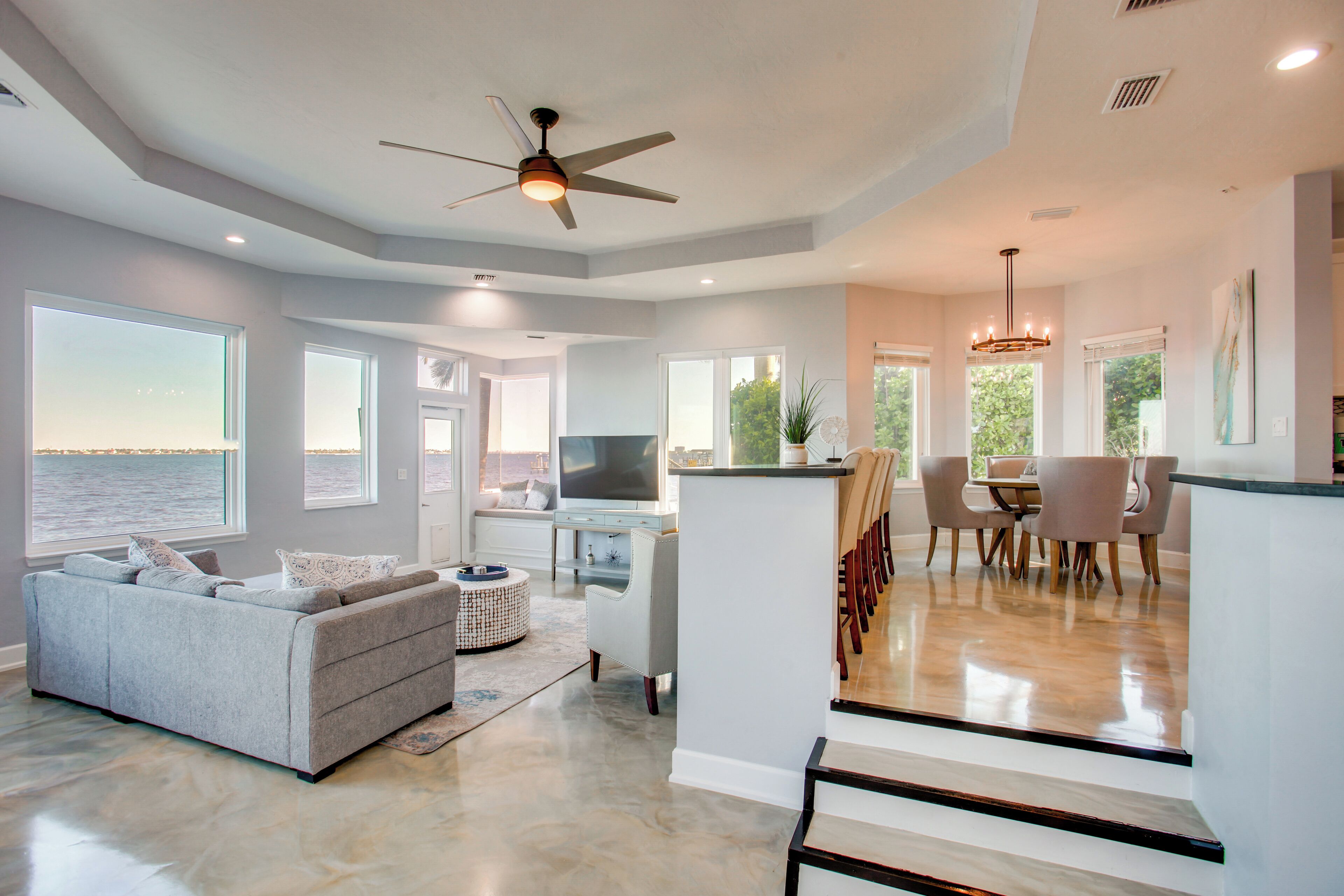 A spacious living area with a grey sofa, a flat-screen TV, and a dining area with a chandelier.