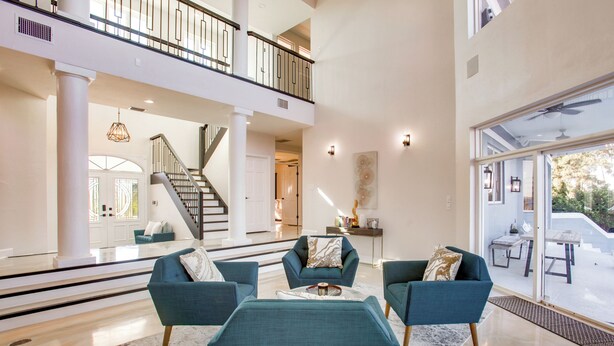 A spacious living area with a high ceiling, a staircase, and a balcony with outdoor furniture. - Riverfront Fort Myers Luxury Home w/ Heated Pool! (Fort Myers)